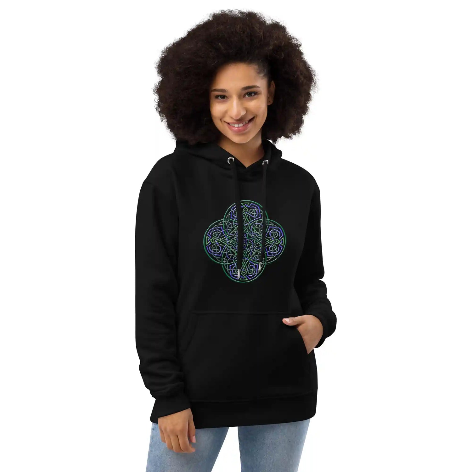 A young woman wearing a black Xigfireon graphic eco-friendly hoodie featuring the Living Colour iteration of the Reach Of The Spirit Celtic knot design. The Reach Of The Spirit Celtic knot symbolizes the Earth.