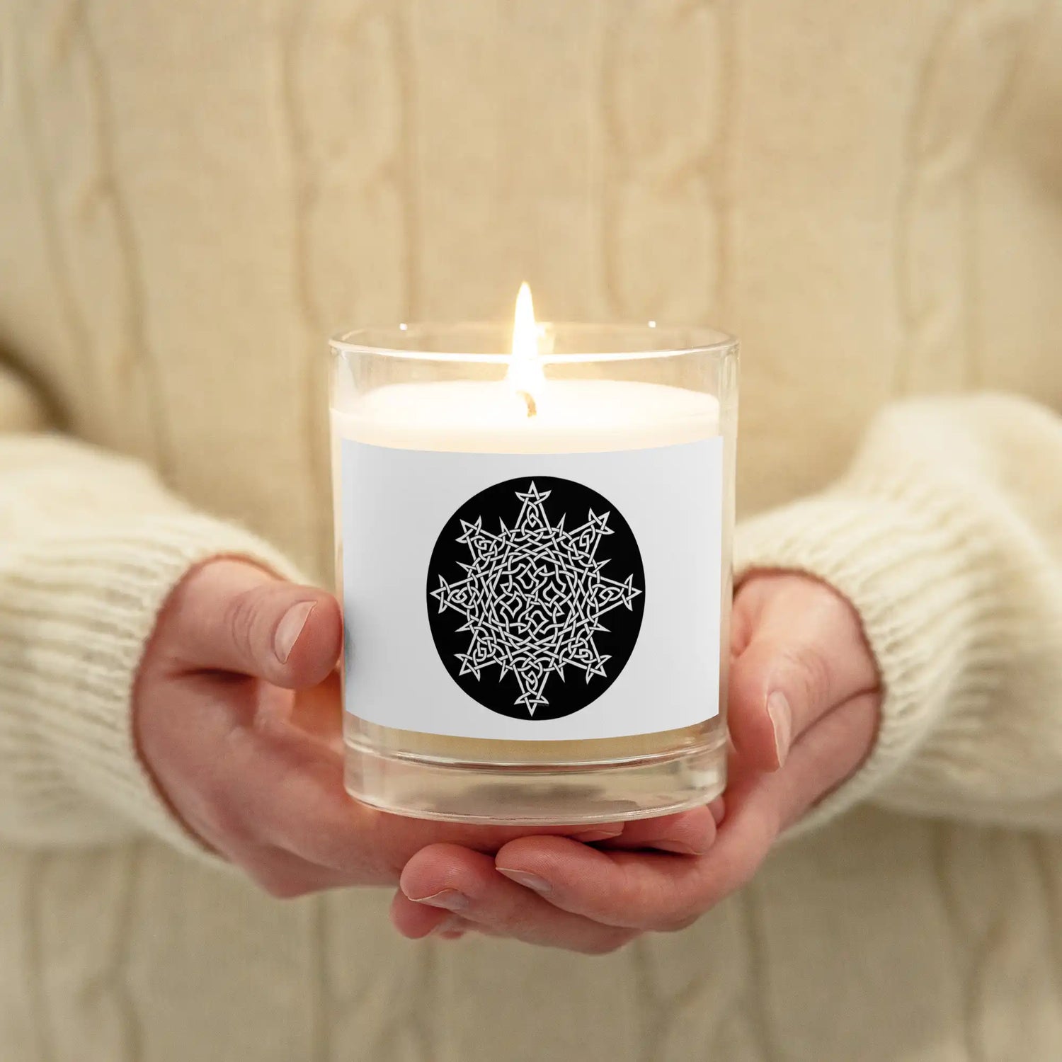 A person holding a Xigfireon glass jar soy wax candle featuring the Black & White Circle iteration of the Morning Star Fire Celtic knot design. The Morning Star Fire Celtic knot symbolizes Father Sun.