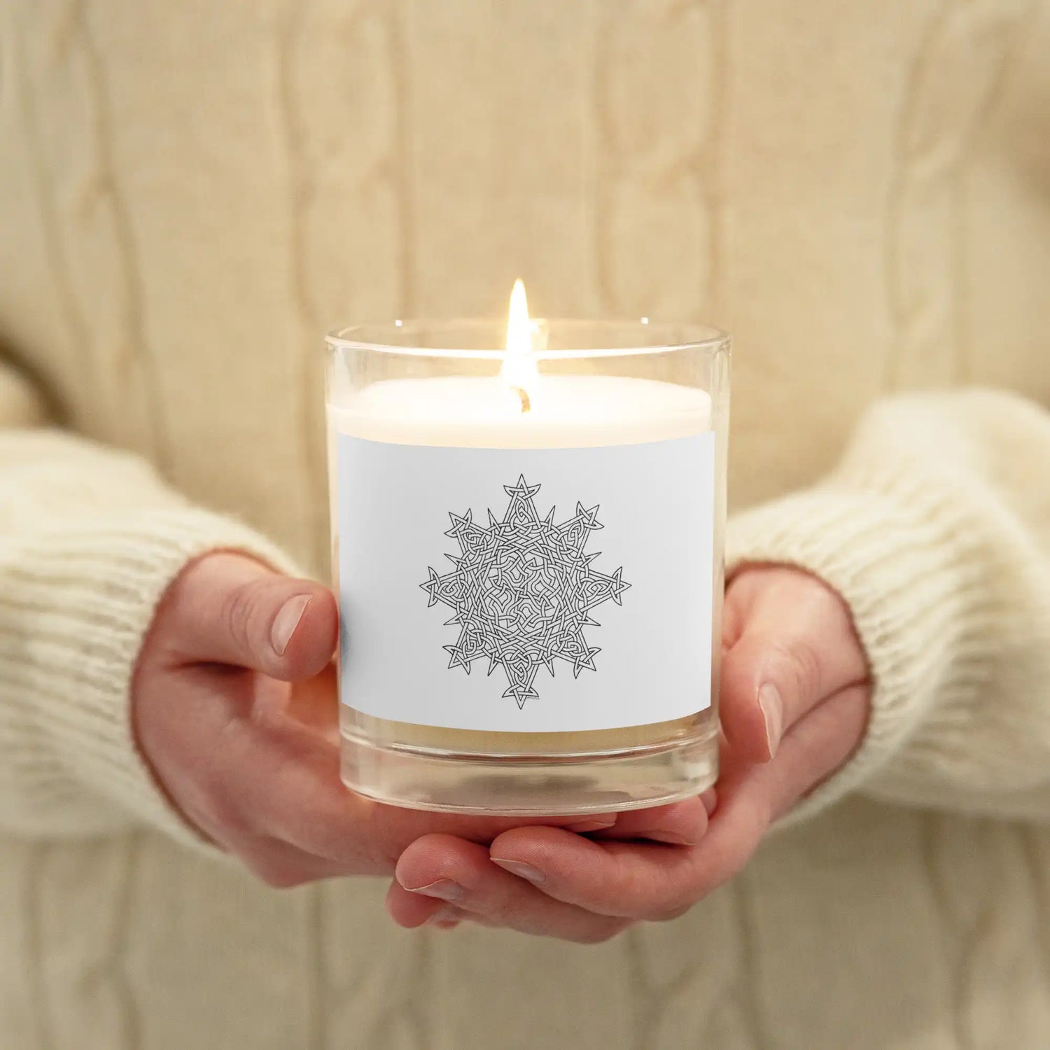A person holding a Xigfireon glass jar soy wax candle featuring the Black & White Hollow iteration of the Morning Star Fire Celtic knot design. The Morning Star Fire Celtic knot symbolizes Father Sun.