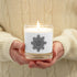 A person holding a Xigfireon glass jar soy wax candle featuring the Black & White Solid iteration of the Morning Star Fire Celtic knot design. The Morning Star Fire Celtic knot symbolizes Father Sun.