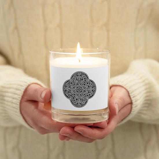 A person holding a Xigfireon glass jar soy wax candle featuring the Black & White Solid iteration of the Reach Of The Spirit Celtic knot design. The Reach Of The Spirit Celtic knot symbolizes Mother Earth.