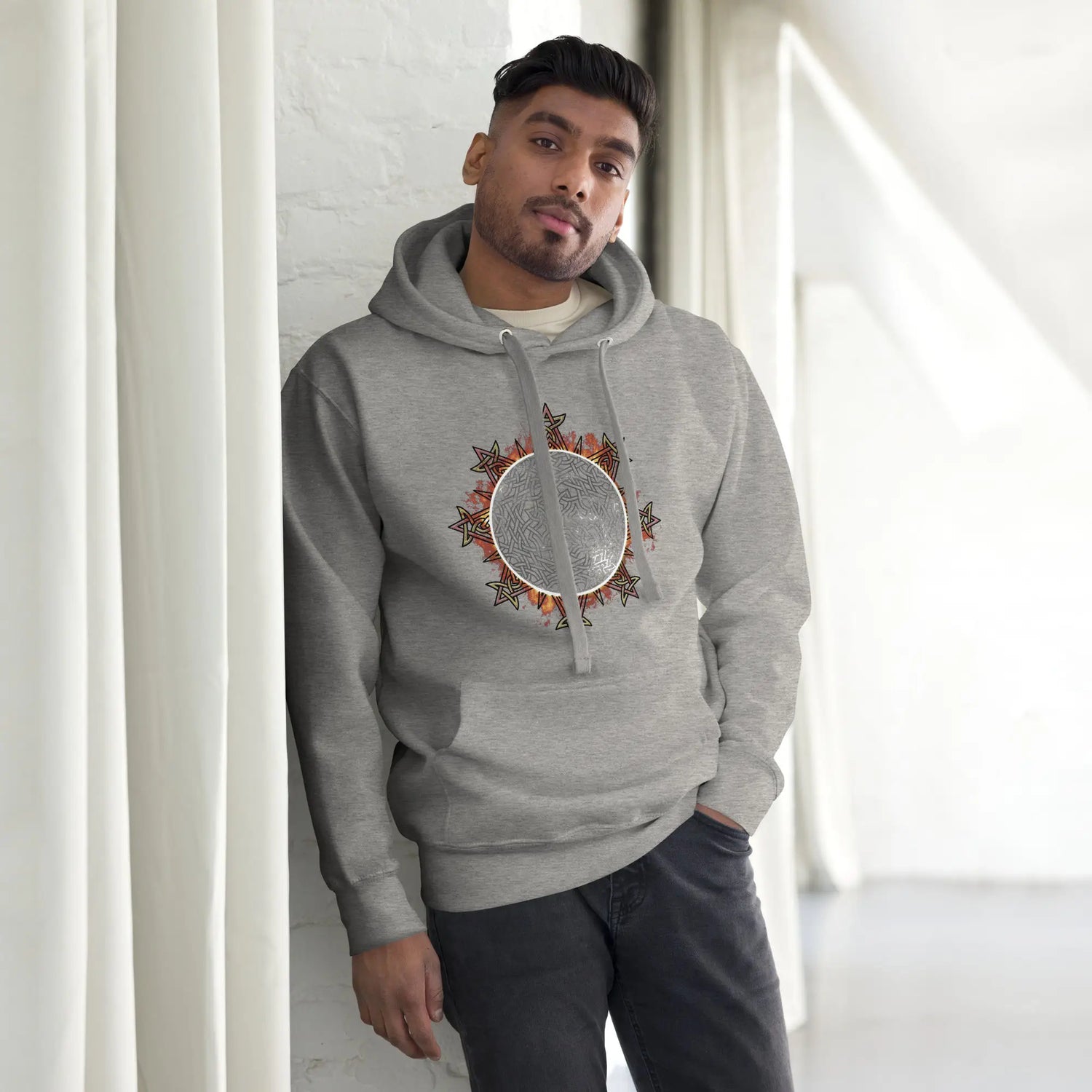 A young man wearing a carbon grey Xigfireon graphic hoodie featuring the Eclipsed iteration of the Morning Star Fire Celtic knot design, inspired by the 2023 Annular Solar Eclipse.