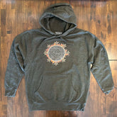 A wooden tabletop with a charcoal heather Xigfireon graphic hoodie featuring the Eclipsed iteration of the Morning Star Fire Celtic knot design, inspired by the 2023 Annular Solar Eclipse.