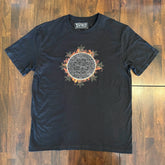 A wooden tabletop with a classic black Xigfireon graphic tee featuring the Eclipsed iteration of the Morning Star Fire Celtic knot design, inspired by the Annular Solar Eclipse of 2023.