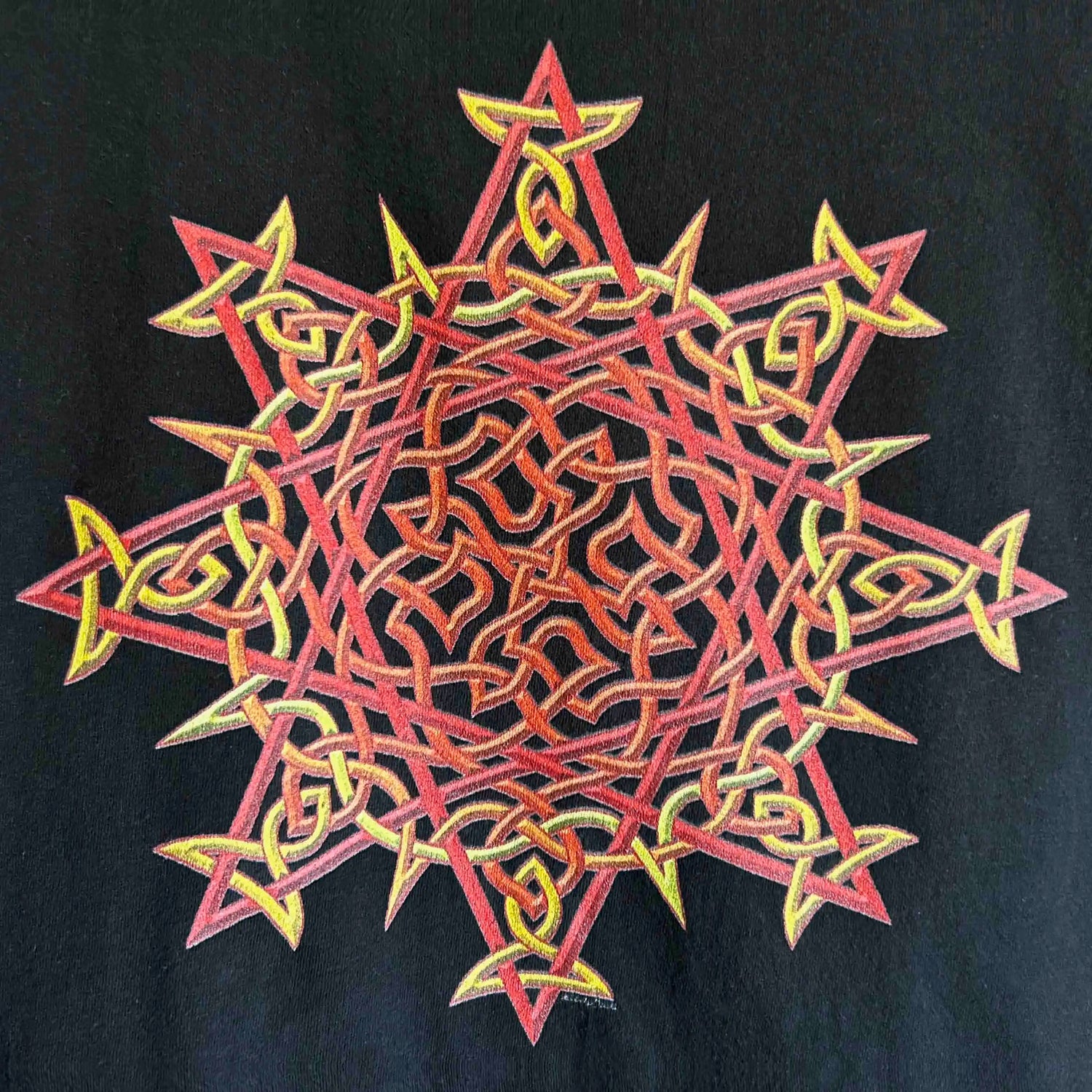 A close-up view of a black Xigfireon graphic t-shirt featuring the Fire Colour iteration of the Morning Star Fire Celtic knot design. The Morning Star Fire Celtic knot represents Father Sun and the eternal Cosmic Light.