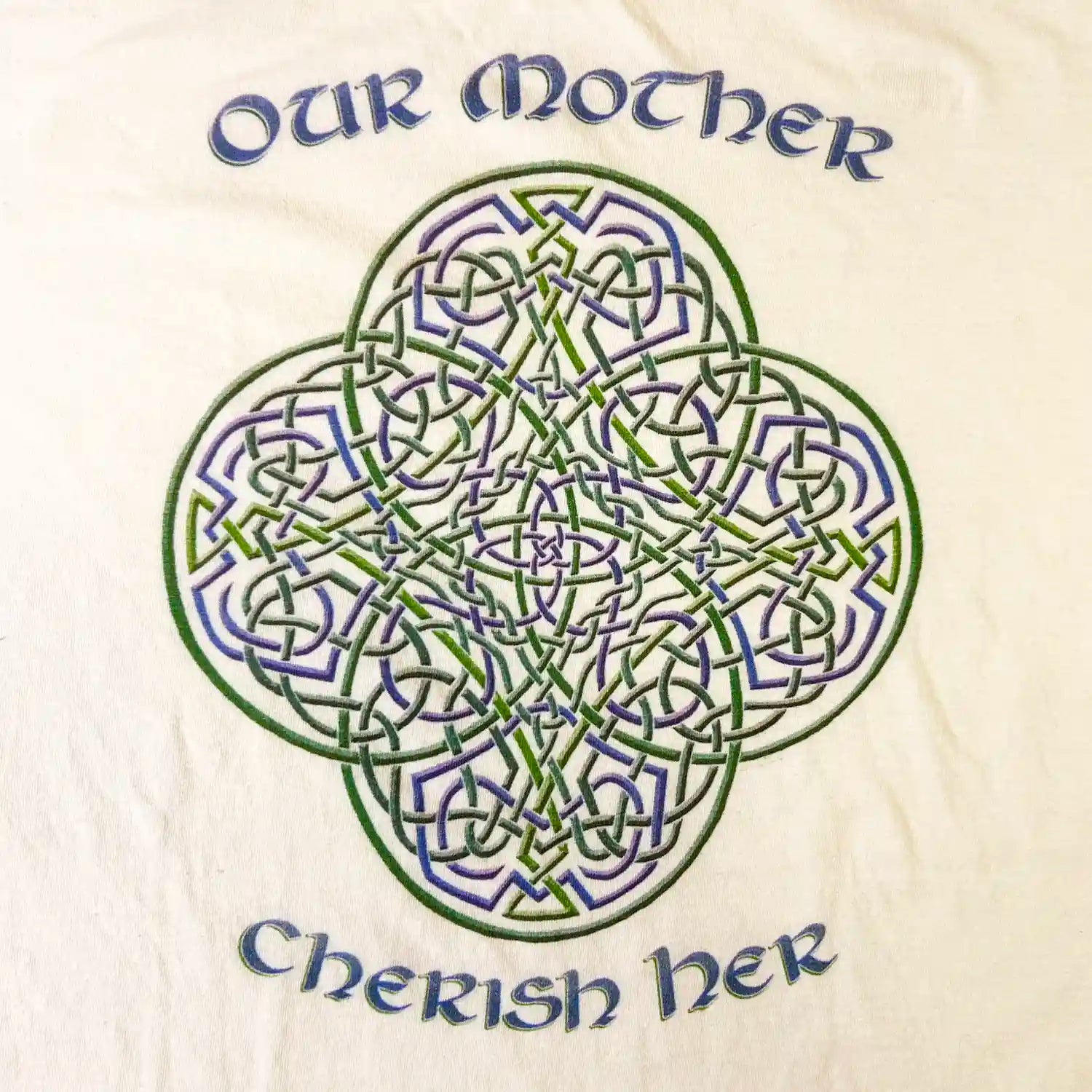 A close up of a white Xigfireon graphic t-shirt featuring the Living Colour iteration of the `Reach Of The Spirit` Celtic knot design along with a message in a Celtic font: "Our Mother, Cherish Her".