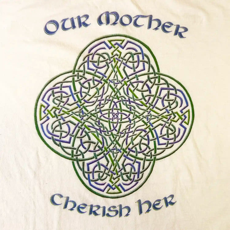 A close up of a white Xigfireon graphic t-shirt featuring the Living Colour iteration of the `Reach Of The Spirit` Celtic knot design along with a message in a Celtic font: "Our Mother, Cherish Her".