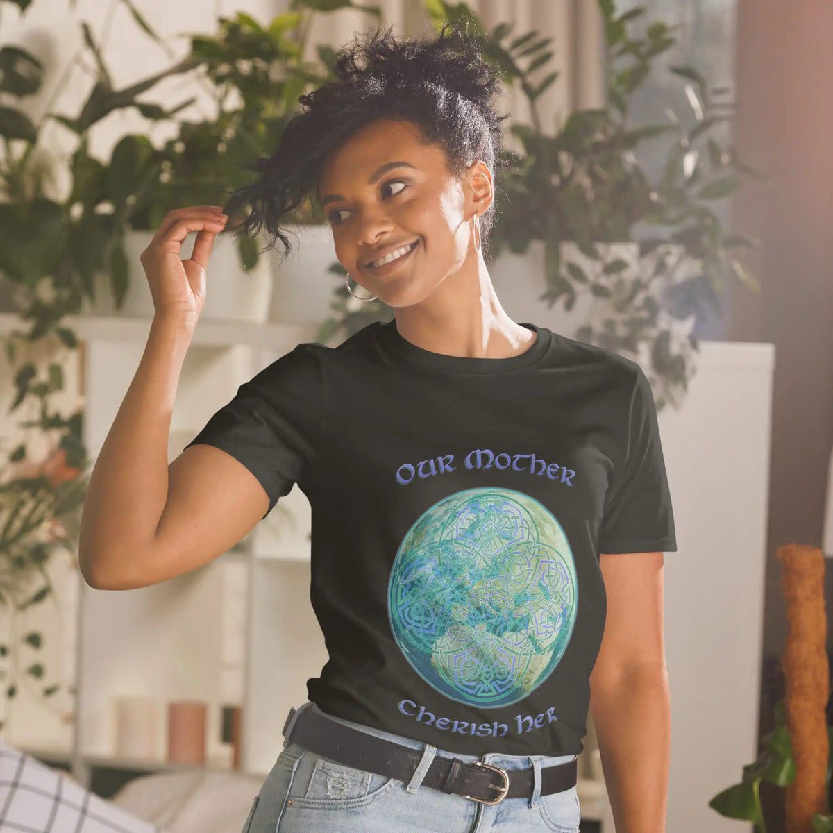 A young woman wearing a black Xigfireon graphic t-shirt featuring the Sacred Planet iteration of the Reach Of The Spirit Celtic knot design along with a message in a Celtic font: "Our Mother, Cherish Her".