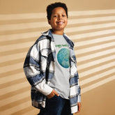 A young boy wearing a kids sport grey graphic t-shirt featuring the Sacred Planet iteration of the `Reach Of The Spirit` Celtic knot design under a message reading "Happy Earth Day".