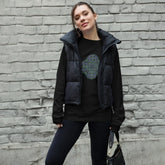 A young woman wearing a black Xigfireon long sleeve graphic t-shirt featuring the Living Colour iteration of the Reach Of The Spirit Celtic knot design. The Reach Of The Spirit Celtic knot symbolizes Mother Earth.