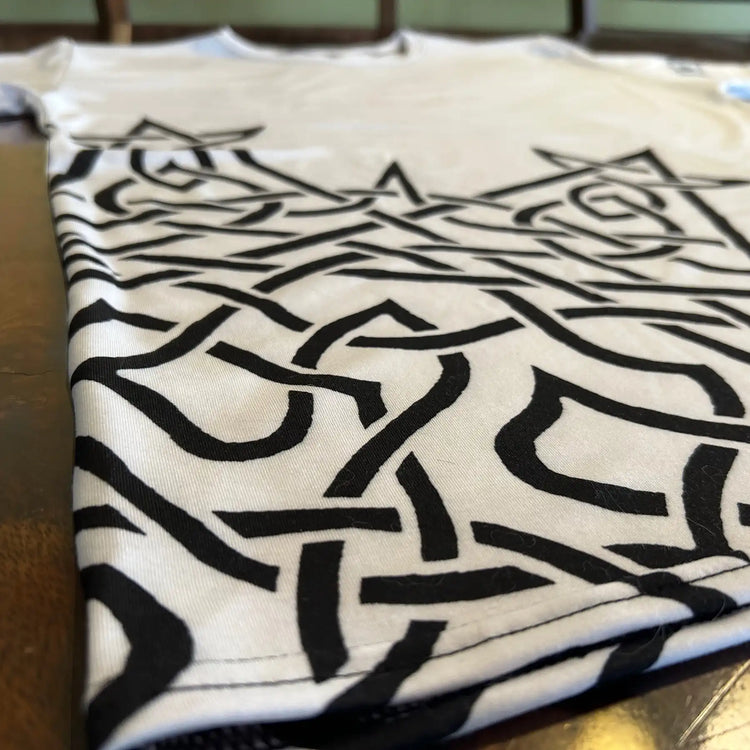 An angled view, from the bottom right side, of a white Xigfireon graphic mens t-shirt featuring the Black Sunset iteration of the Morning Star Fire Celtic knot design.