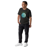 A young man wearing a dark heather grey organic graphic t-shirt featuring the Sacred Planet iteration of the Reach Of The Spirit Celtic knot design under a message reading "Happy Earth Day".