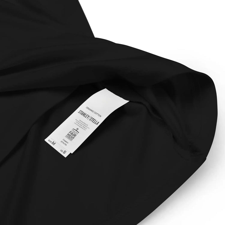 A close-up view of a product tag on a black Xigfireon graphic organic cotton t-shirt featuring the Deep Forest iteration of the Reach Of The Spirit Celtic knot design. The Reach Of The Spirit Celtic knot represents the glorious Earth.