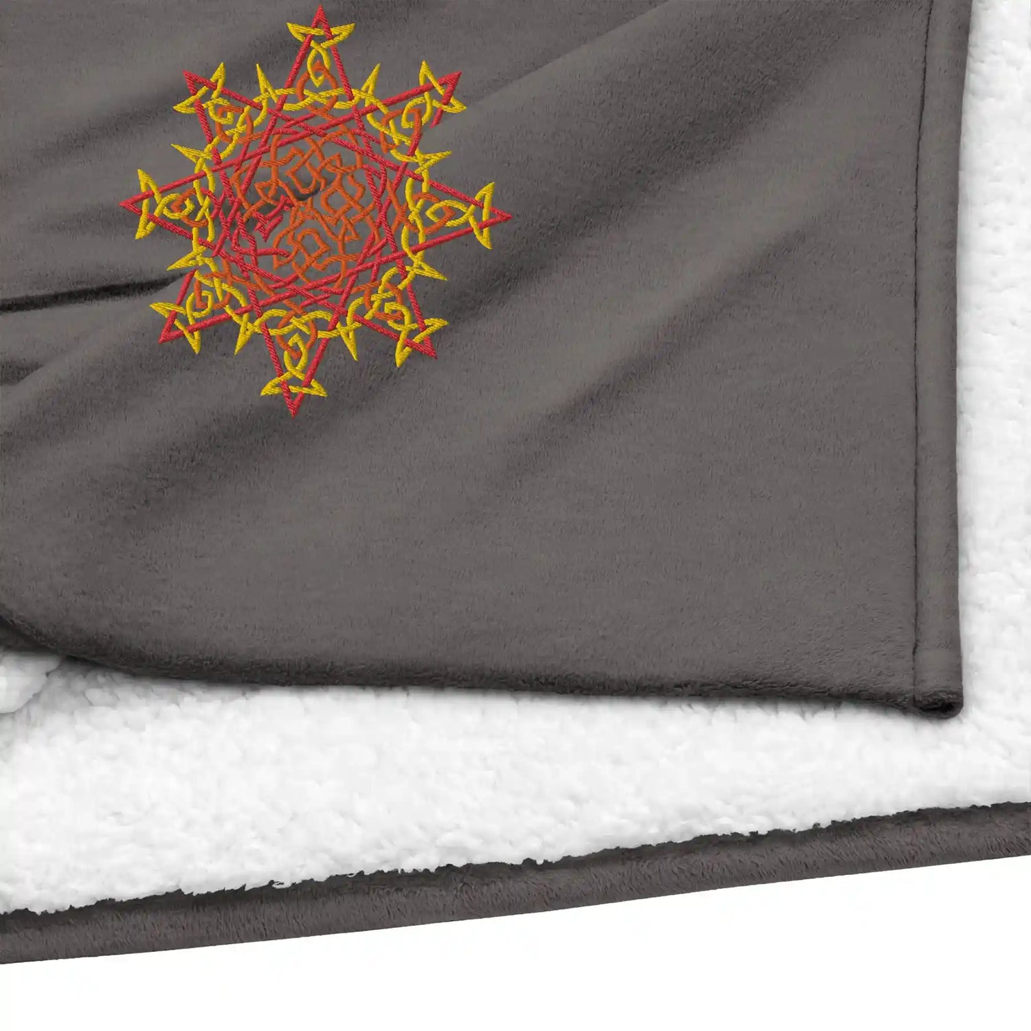 A close-up view of a heather grey Xigfireon sherpa blanket embroidered with the Fire Colour iteration of the Morning Star Fire Celtic knot design.