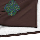 A close-up view of a fireside brown Xigfireon sherpa blanket embroidered with the Living Colour iteration of the Reach Of The Spirit Celtic knot design.