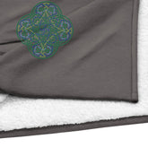 A close-up view of a heather grey Xigfireon sherpa blanket embroidered with the Living Colour iteration of the Reach Of The Spirit Celtic knot design.