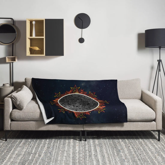 A sofa covered by a 50 inch by 60 inch Xigfireon throw blanket featuring the Eclipsed iteration of the Morning Star Fire Celtic knot design. Inspired by the 2023 Annular Solar Eclipse.
