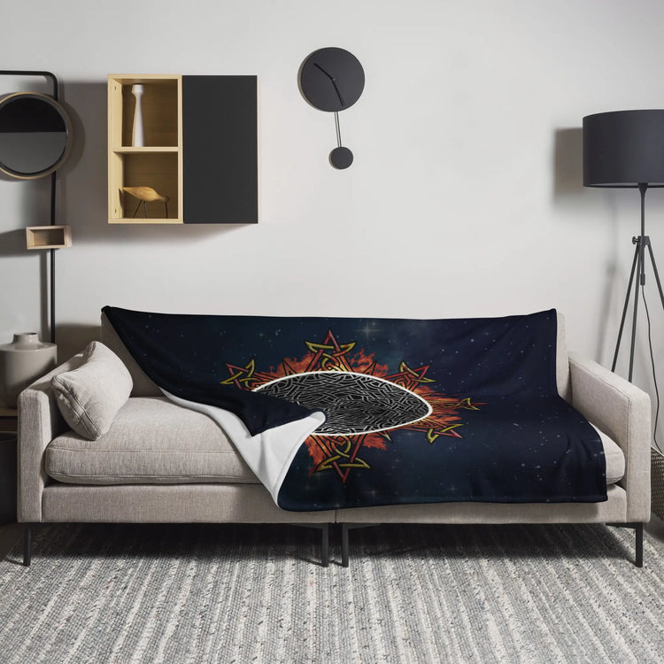 A sofa covered by a 60 inch by 80 inch Xigfireon throw blanket featuring the Eclipsed iteration of the Morning Star Fire Celtic knot design. Inspired by the 2023 Annular Solar Eclipse.