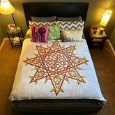 A bed that is covered with a Xigfireon throw blanket featuring the original blazing Fire Colour iteration of the Morning Star Fire Celtic knot design. The Morning Star Fire Celtic knot represents the Sun.