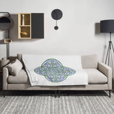A sofa covered by a 50 inch by 60 inch Xigfireon throw blanket featuring the original Living Colour iteration of the Reach Of The Spirit Celtic knot design. The Reach Of The Spirit Celtic knot represents the Earth.