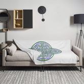A sofa covered by a 60 inch by 80 inch Xigfireon throw blanket featuring the original Living Colour iteration of the Reach Of The Spirit Celtic knot design. The Reach Of The Spirit Celtic knot represents the Earth.