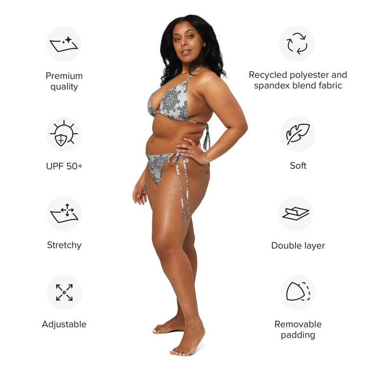 A list of product features surrounding a woman wearing a string bikini featuring the Inverted Black & White Solid Cosmos iteration of the Morning Star Fire Celtic knot pattern. Features include premium quality, recycled polyester and spandex blend fabric, UPF 50+, soft, stretchy, double layer, adjustable, and removable padding.