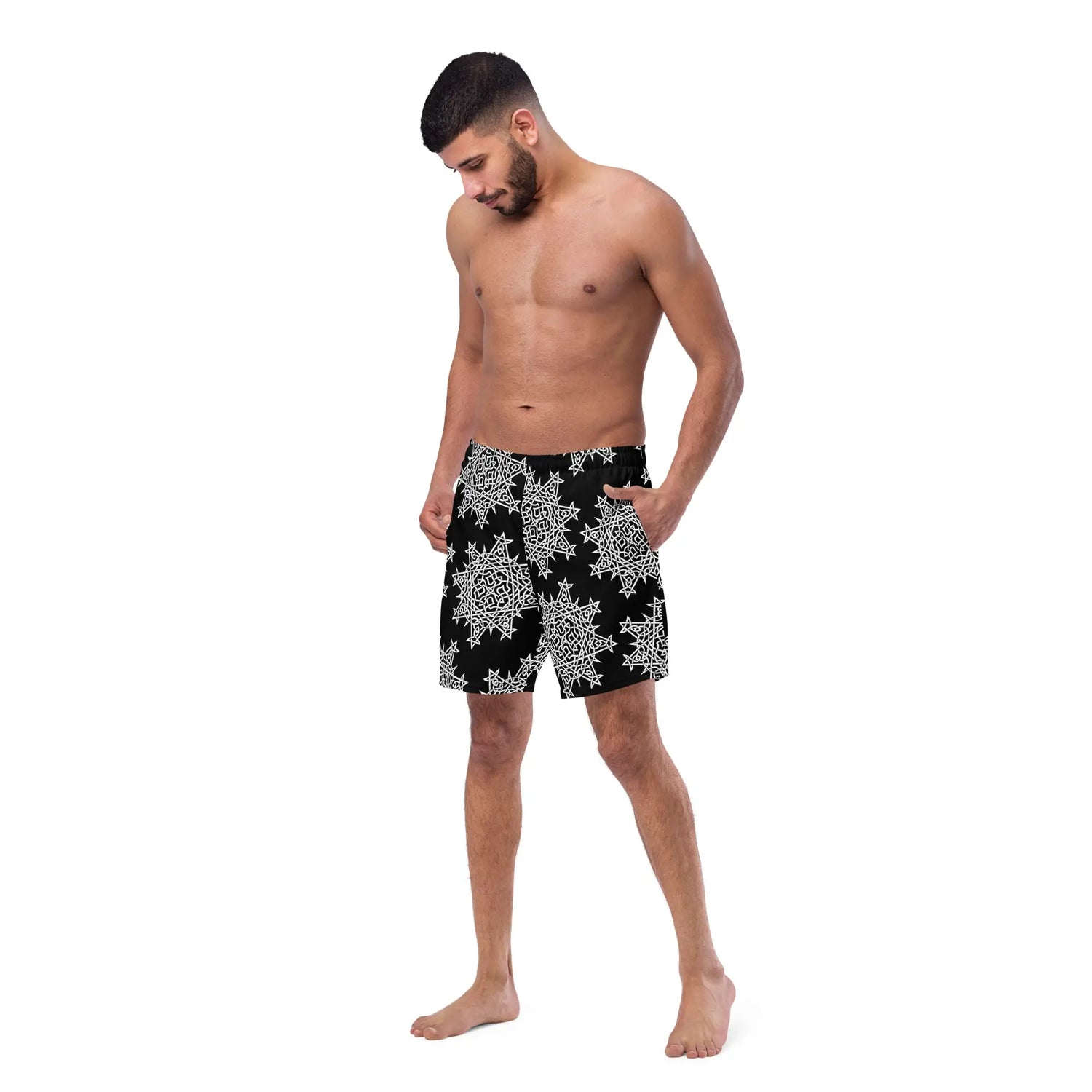 A young man wearing a pair of Xigfireon graphic swim trunks featuring the Black & White Solid Black patterned series of the Morning Star Fire Celtic knot design.