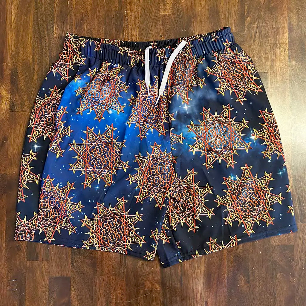 A pair of swim trunks featuing the Fire Colour Cosmos patterns of the Morning Star Fire Celtic knot, shown laying flat on a wooden table.