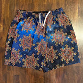 A pair of swim trunks featuing the Fire Colour Cosmos patterns of the Morning Star Fire Celtic knot, shown laying flat on a wooden table.
