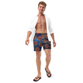 A young man wearing a pair of Xigfireon graphic swim trunks featuring the Fire Colour Cosmos (small) patterned series of the Morning Star Fire Celtic knot design.