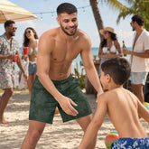 A man playing with his son at a beach party. The man is wearing a pair of Xigfireon swim trunks featuring the Midnight Cosmos version of the `Morning Star Fire` Celtic knot pattern.