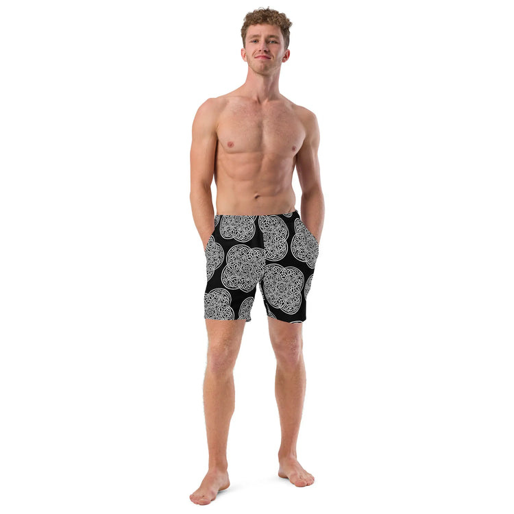 A young man wearing a pair of Xigfireon graphic swim trunks featuring the Black & White Solid Black patterned series of the Reach Of The Spirit Celtic knot design.