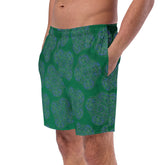 A young man wearing a pair of Xigfireon graphic swim trunks featuring the Living Colour Forest (small) patterned series of the Reach Of The Spirit Celtic knot design.