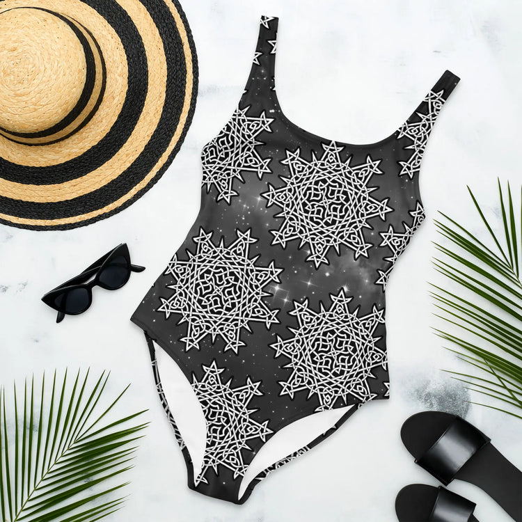 A sunhat, sun glasses, and beach sandals displayed with a Xigfireon graphic swimsuit featuring the Black & White Solid Cosmos patterned series of the Morning Star Fire Celtic knot design.