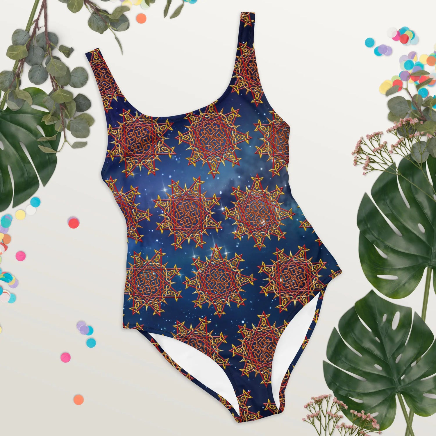 Some tropical plant leaves surrounding a Xigfireon graphic swimsuit featuring the Fire Colour Solid Cosmos (small) patterned series of the Morning Star Fire Celtic knot design.