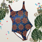 Some tropical plant leaves surrounding a Xigfireon graphic swimsuit featuring the Fire Colour Solid Cosmos (small) patterned series of the Morning Star Fire Celtic knot design.