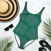 A sunhat, sun glasses, and beach sandals displayed with a Xigfireon graphic swimsuit featuring the Living Colour Forest patterned series of the Reach Of The Spirit Celtic knot design.