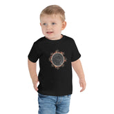 A young boy shown wearing a black Xigfireon toddler graphic t-shirt featuring the Eclipsed iteration of the `Morning Star Fire` Celtic knot design. The `Morning Star Fire` Celtic knot represents the Sun.