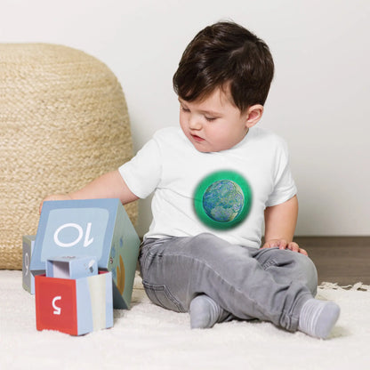 A young boy shown wearing a white Xigfireon toddler graphic t-shirt featuring the Deep Forest iteration of the Reach Of The Spirit Celtic knot design. The Reach Of The Spirit Celtic knot symbolizes Mother Earth.