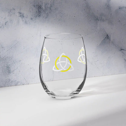 The front side of a stemless wine glass featuring the White &amp; Yellow iteration of the Trinity Knot design shown on a counter in front of a textured wall. Also referred to as the triquetra, the Trinity Knot has long symbolized unity and balance.
