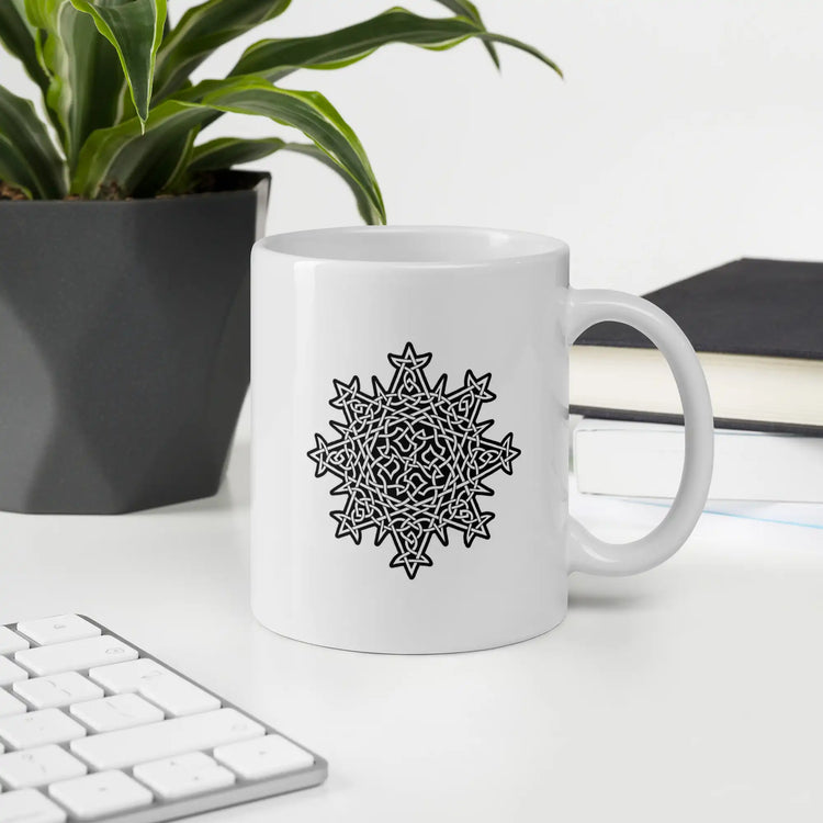A desktop displaying a Xigfireon white glossy 11oz mug featuring the Black & White Solid iteration of the Morning Star Fire Celtic knot design. This Celtic knot symbolizes Father Sun.