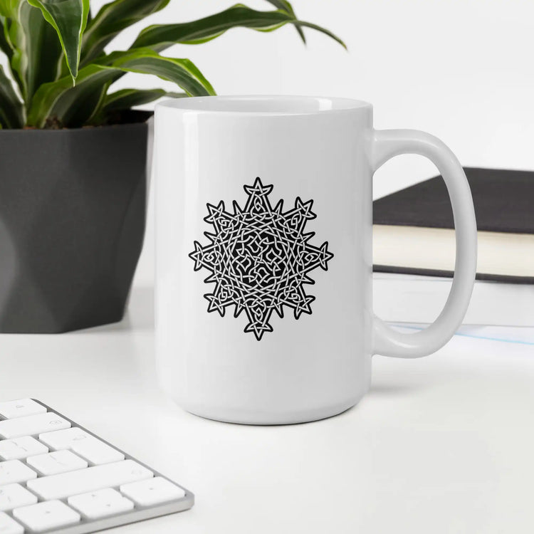 A desktop displaying a Xigfireon white glossy 15oz mug featuring the Black & White Solid iteration of the Morning Star Fire Celtic knot design. This Celtic knot symbolizes Father Sun.