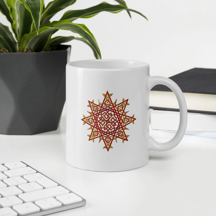 An office desktop displaying a Xigfireon white ceramic 11oz mug featuring the Fire Colour iteration of the Morning Star Fire Celtic knot design. This Celtic knot symbolizes Father Sun.