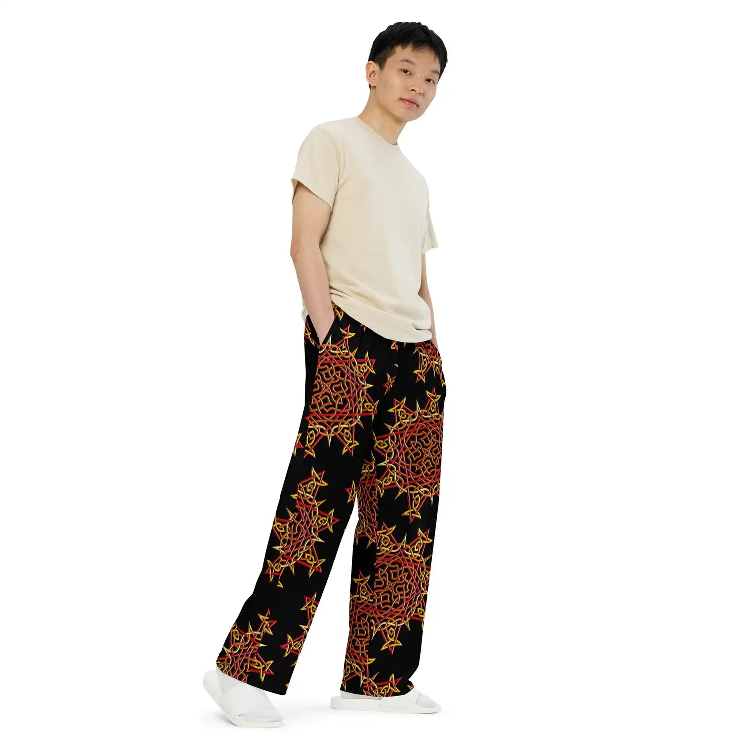 A young man wearing a pair of Xigfireon graphic wide leg pants featuring the Fire Colour Black patterned series of the Morning Star Fire Celtic knot design.