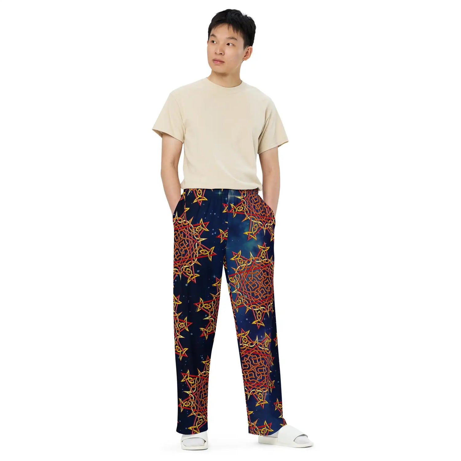 A young man wearing a pair of Xigfireon graphic wide leg pants featuring the Fire Colour Cosmos patterned series of the Morning Star Fire Celtic knot design.