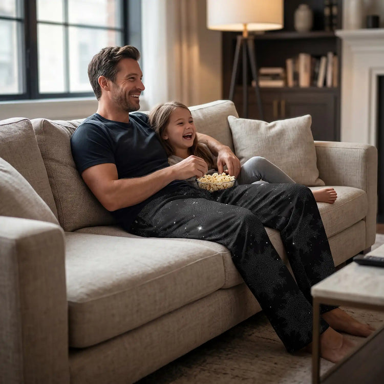 Man and young girl sitting on a couch eating popcorn while watching a movie in a cozy living room. The man is wearing a pair of Xigfireon wide-leg pants featuring the `Morning Star Fire` Midnight Cosmos Celtic knot pattern.