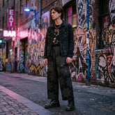 A young man dressed in punk attire, including a black jean jacket, black boots, and a pair of Xigfireon wide-leg pants featuring the Midnight Cosmos `Morning Star Fire` Celtic knot pattern.
