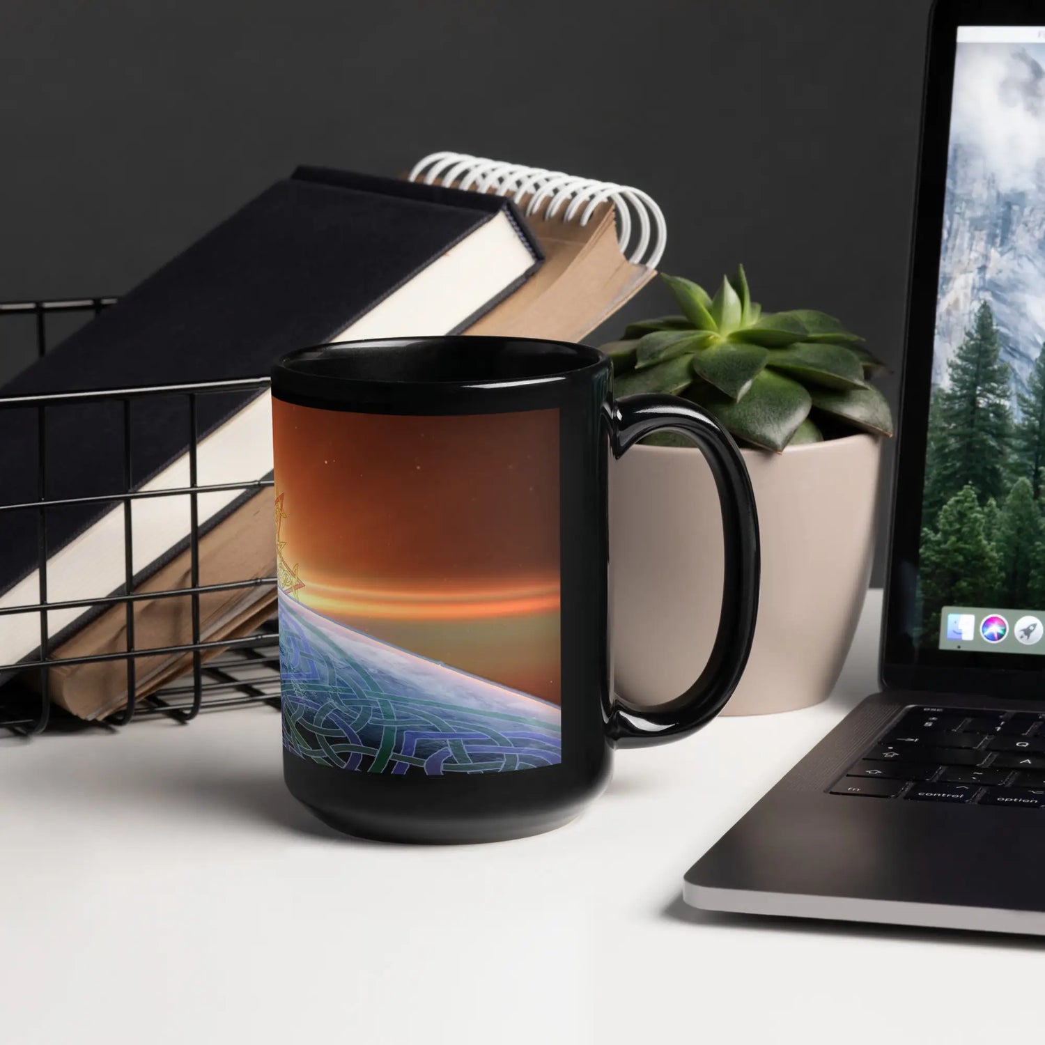 An office desk displaying a 15oz Xigfireon black glossy graphic mug featuring the `Derivation II` Celtic knots merger design.