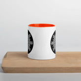 A Xigfireon white ceramic 11oz mug featuring the Black & White Circle iteration of the `Morning Star Fire` Celtic knot design, with orange handle and inside. This Celtic knot symbolizes Father Sun.