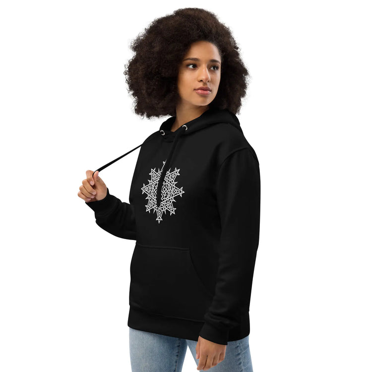 A young woman wearing a black Xigfireon graphic eco hoodie featuring the Black & White Hollow iteration of the `Morning Star Fire` Celtic knot design. The `Morning Star Fire` Celtic knot is a Sun symbol.